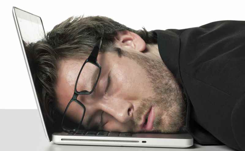 Unmotivated, sleeping employee, with the head on his laptop, eyes closed with glasses