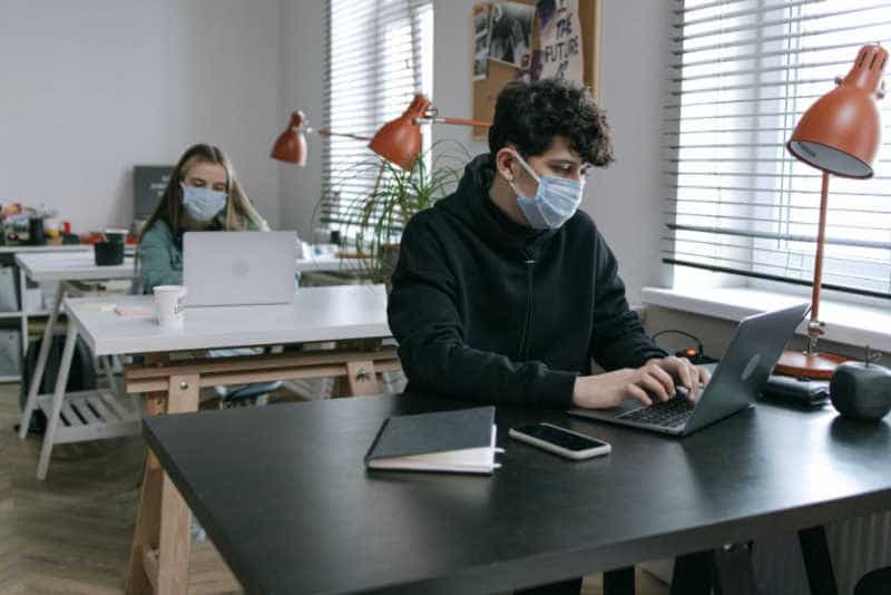 employees working on laptop at their desk wearing masks