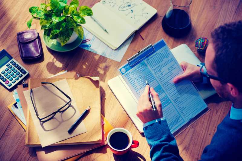 Hipster Man Casually Filing In The Application Form On His Wooden Desk