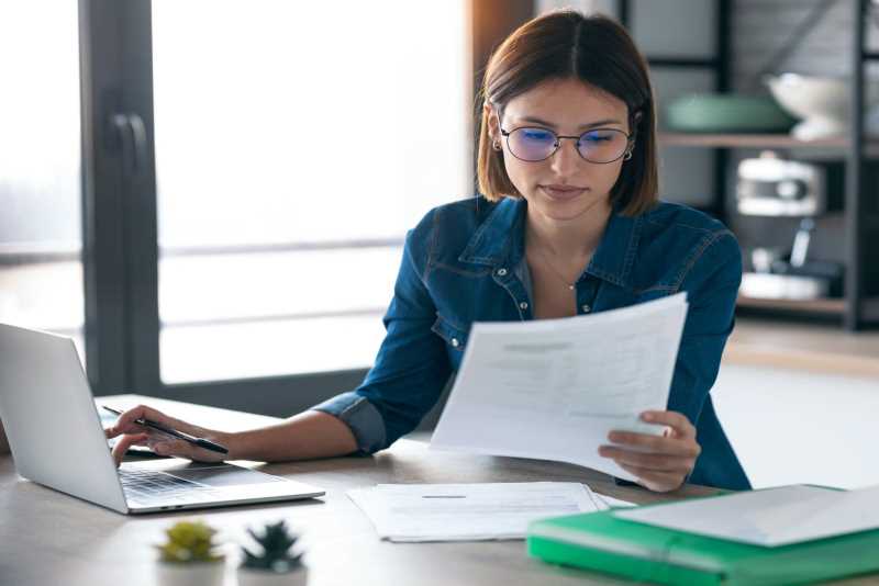 woman reading a document and working on a laptop