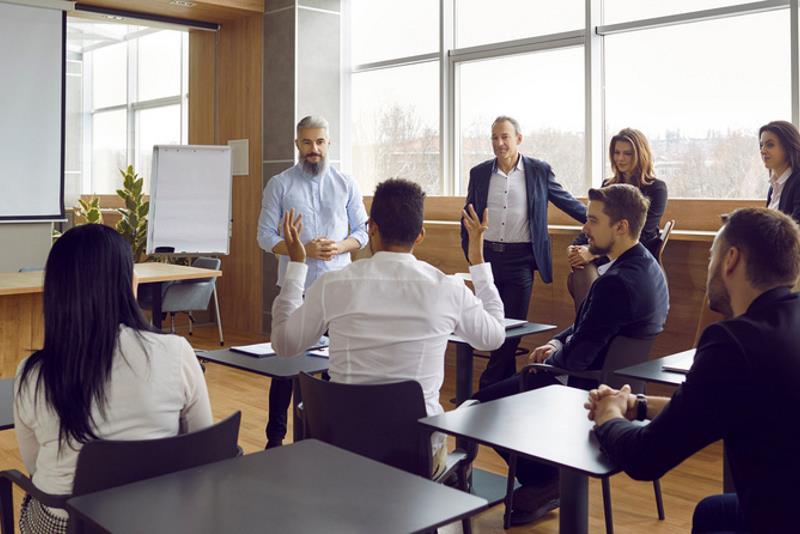 Panoramic view of people office staff standing and sitting at desks in modern office talking during break on corporate team training. Multiracial group men and women discussing seminar or masterclass.