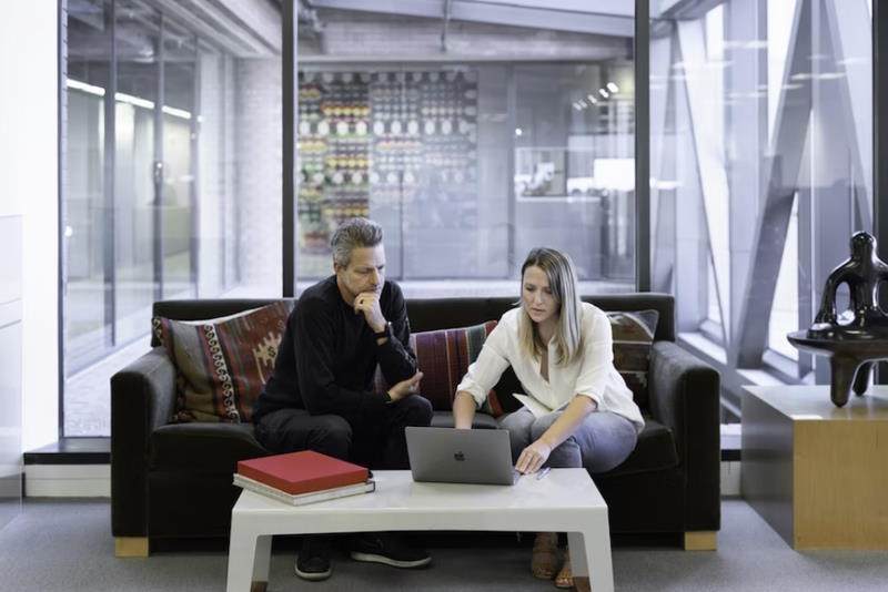 2 people sitting in a sofa working on a laptop