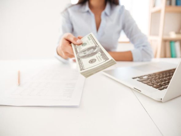 woman sitting at a desk handlling over banknotes near an open laptop