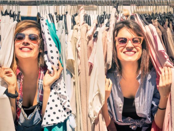 two women smiling surrounded by clothes on hangers